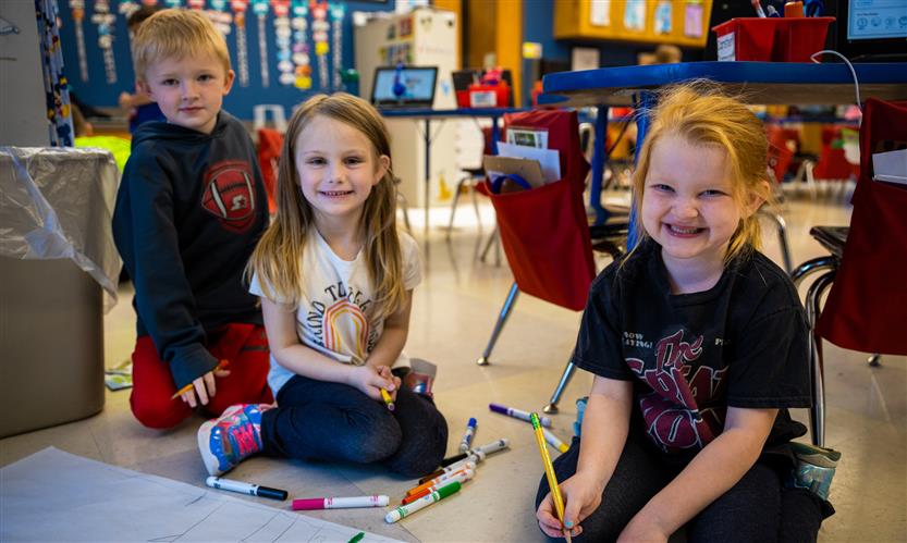 Three students smile while working on a paper mural